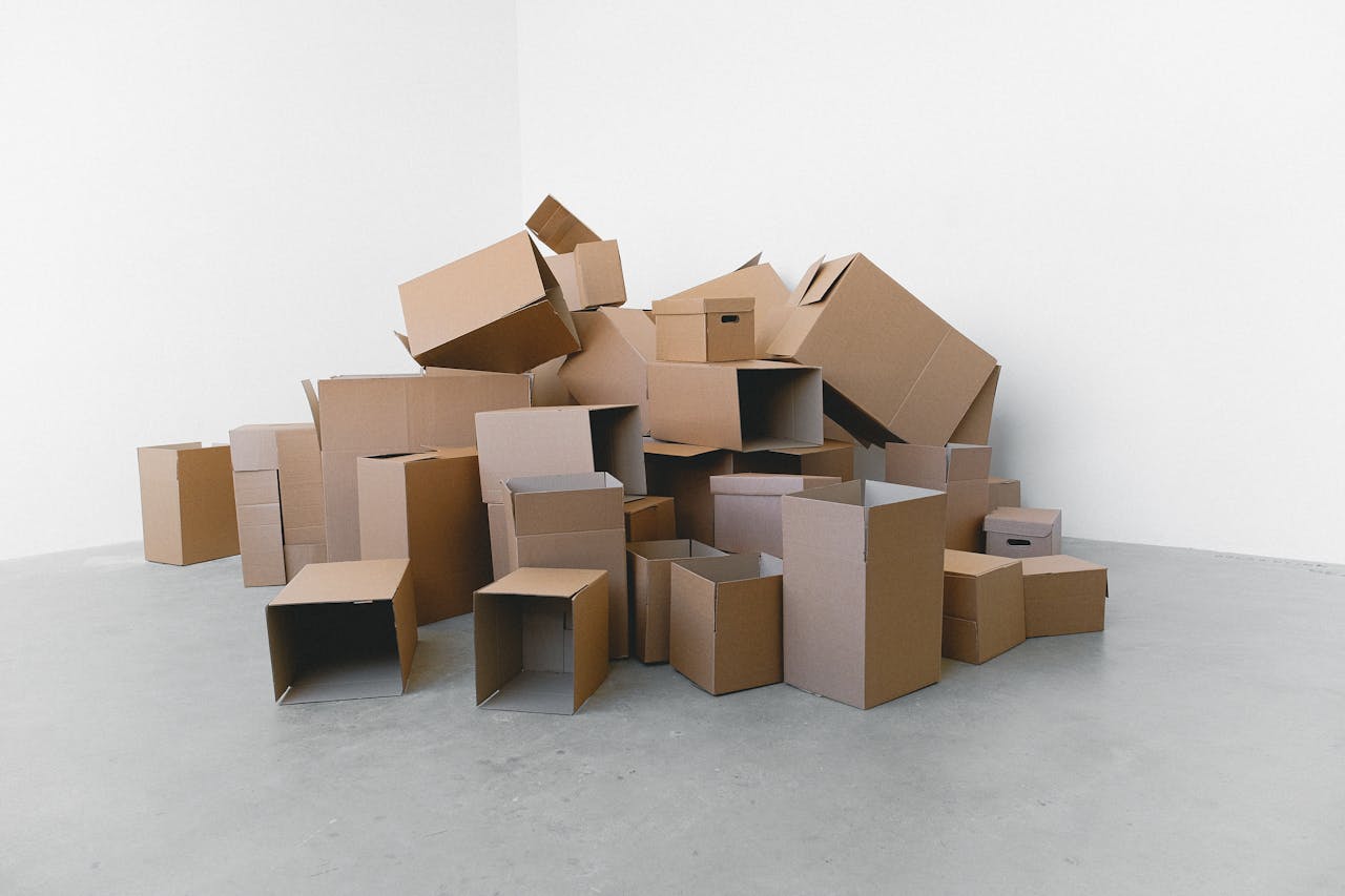 A pile of empty cardboard boxes arranged on a grey floor against a white wall, perfect for moving themes.